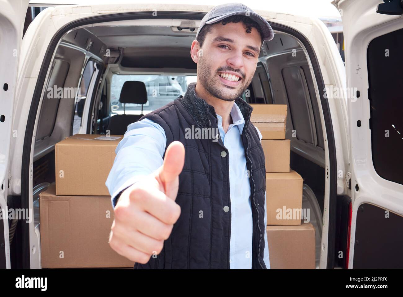 Un service de qualité est ma promesse à vous. Portrait d'un jeune liveur montrant les pouces vers le haut tout en chargeant des boîtes d'une camionnette. Banque D'Images