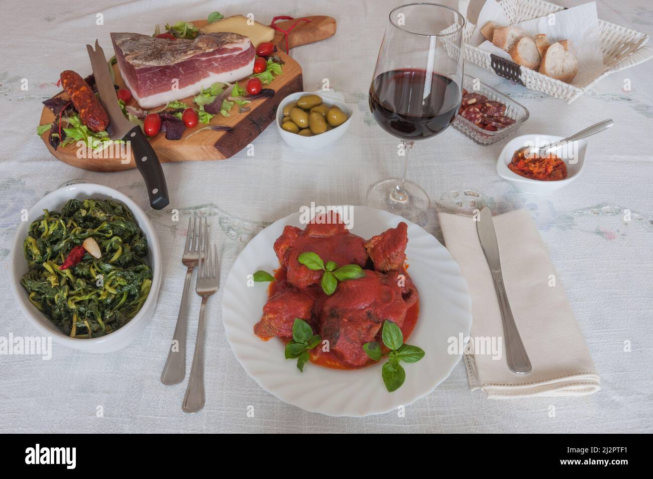 Cuisine italienne: Table avec ragoût de viande (ragù napoletano) avec basilic, brocoli, speck, salami, olives, pain, sauce chili et vin rouge. avec basilic, Banque D'Images