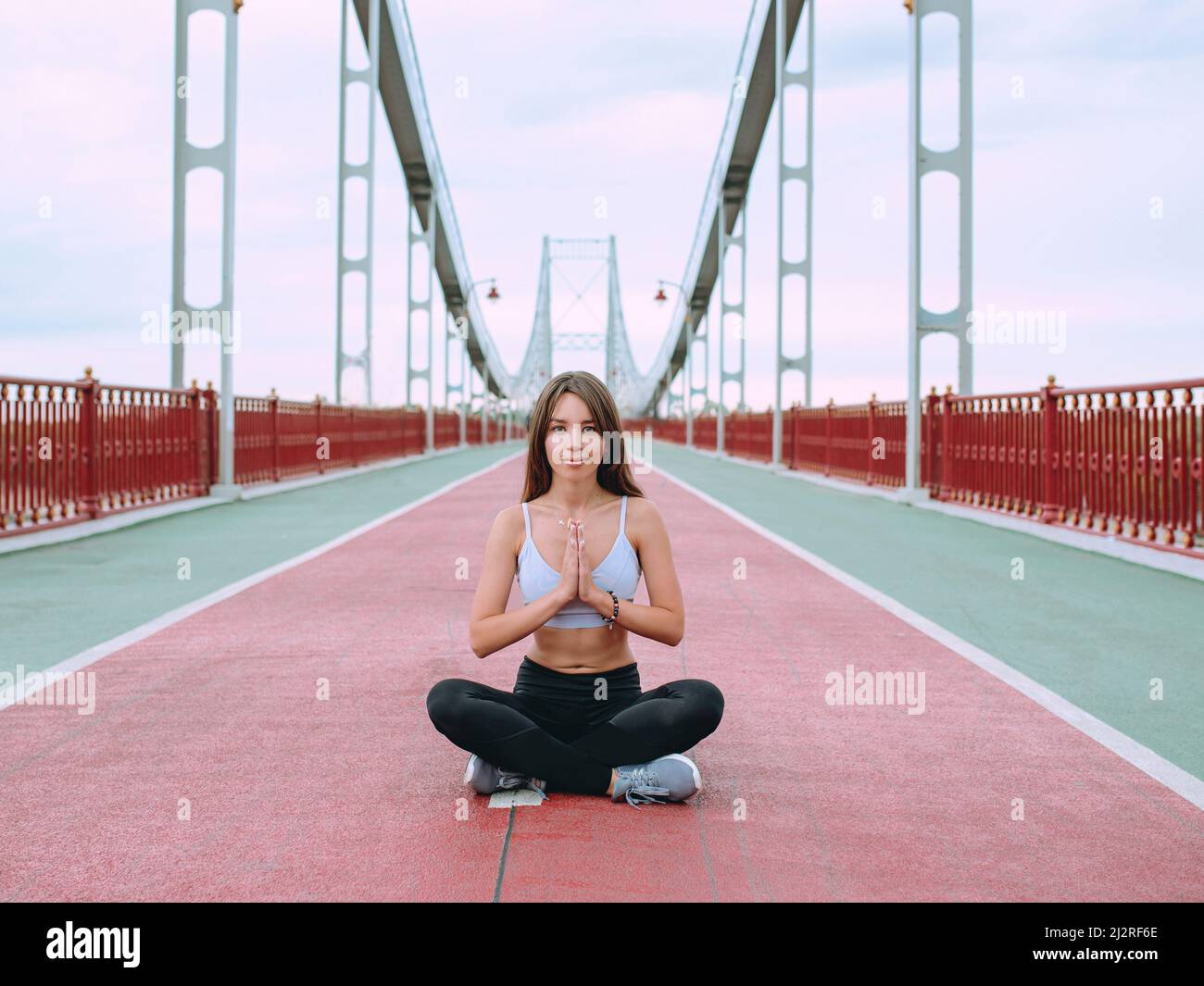 belle, sportive, en forme, jeune femme caucasienne dans les vêtements de sport et les baskets assis à lotus pose sur le pont. Sport, activité, yoga, style de vie urbain c Banque D'Images