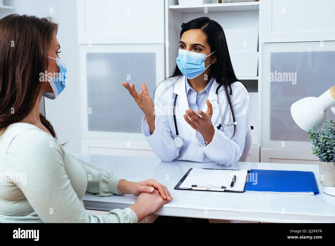Médecin et patient dans le masque de visage discutant des problèmes de santé tout en étant assis à la table dans le centre médical de l'industrie de la santé Banque D'Images