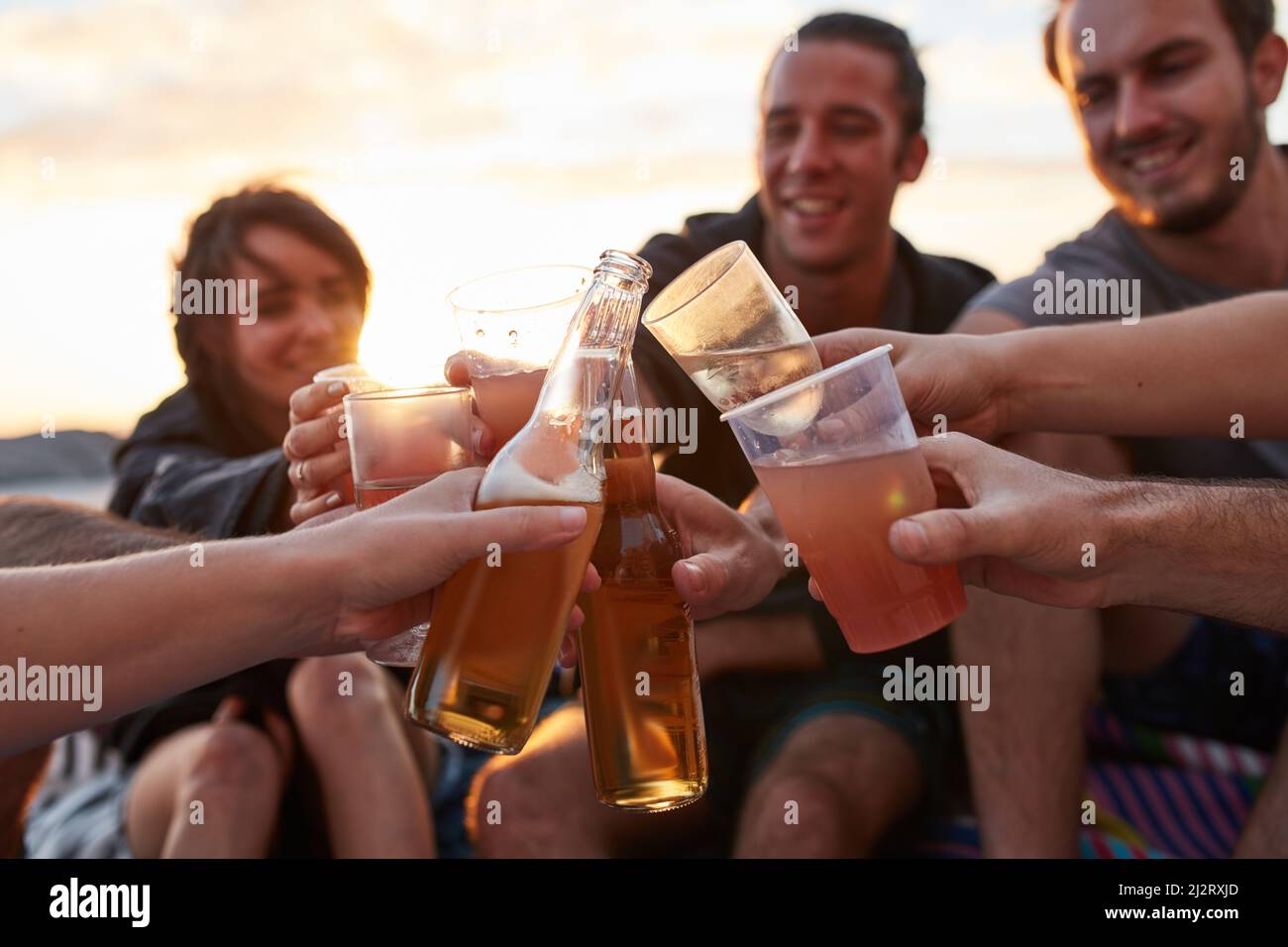 Jeune, sauvage et libre. Prise de vue d'un groupe de jeunes amis heureux en dégustant leurs boissons tout en se relaxant sur la plage. Banque D'Images