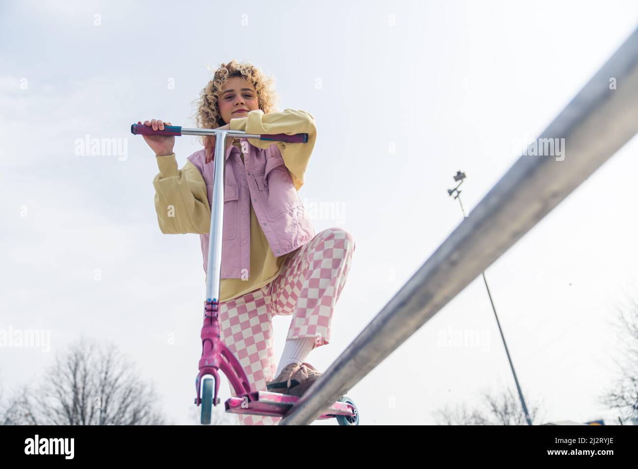 Belle jeune femme blonde posant avec un scooter rose, souriant et regardant la caméra active style de vie concept copier espace moyen plein plan. Photo de haute qualité Banque D'Images