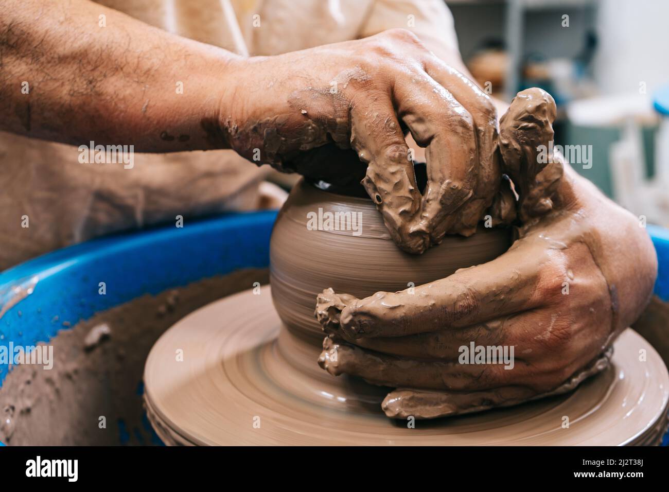 Les mains habiles d'une argile de travail de potier sur une roue de potier. L'argile prend la forme que le potier lui donne avec le ton de terre cuite de l'argile. Banque D'Images