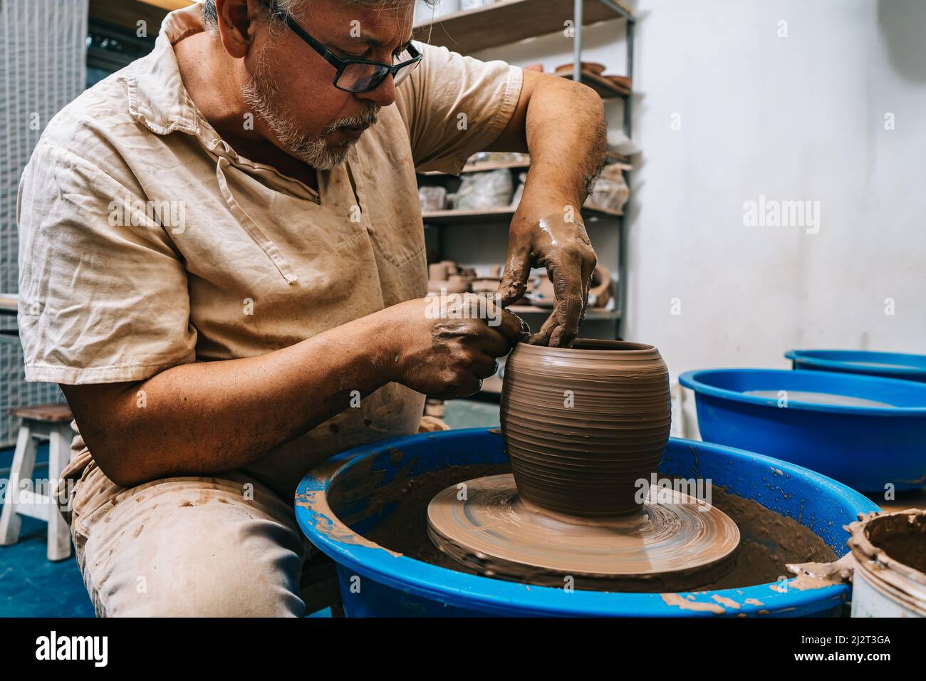 Un potier qualifié travaillant l'argile avec ses mains sur une roue de potier, la façonnant comme il tourne. Concept de fabrication artisanale. Banque D'Images