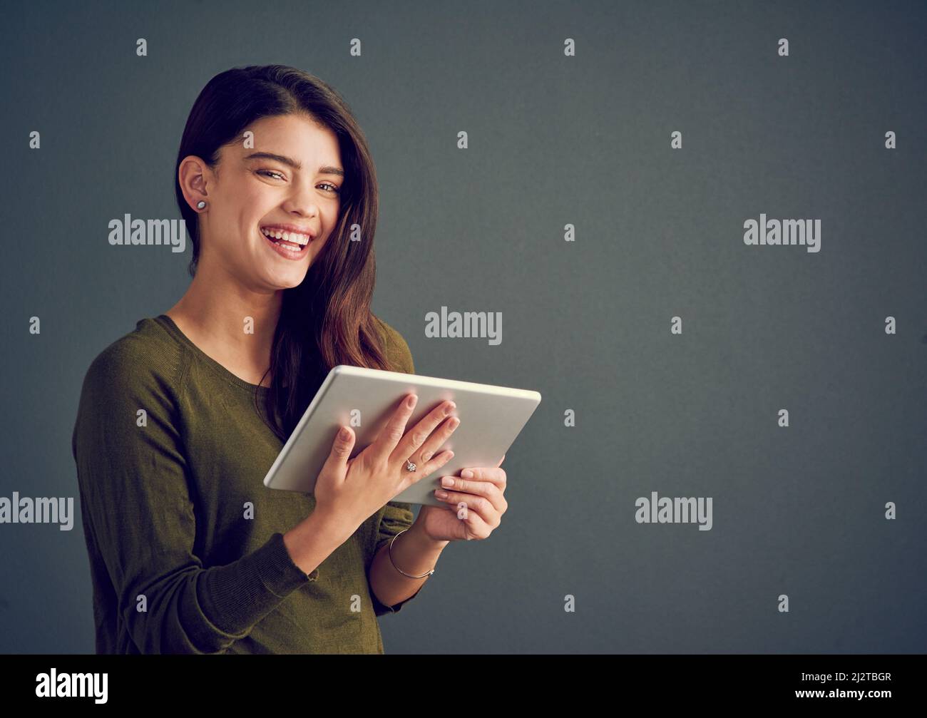 Je peux emporter mon travail partout où je vais. Photo en studio d'une jeune femme joyeuse tenant une tablette numérique sur fond sombre. Banque D'Images