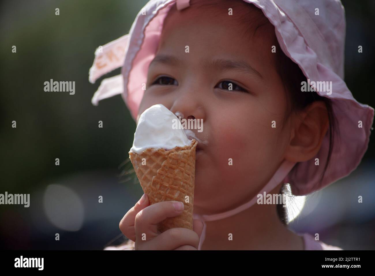 L'enfant mange de la crème glacée. Une fille qui lèche la glace dans la rue. Un cône gaufré dans les mains d'un enfant asiatique. Portrait d'une jolie fille avec un sucre Banque D'Images