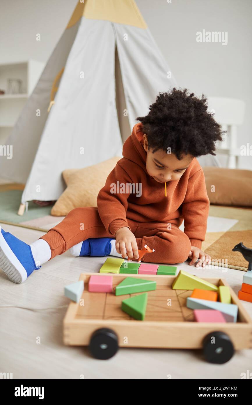 Portrait vertical d'un adorable tout-petit afro-américain jouant avec des jouets en bois dans une chambre confortable pour les enfants Banque D'Images