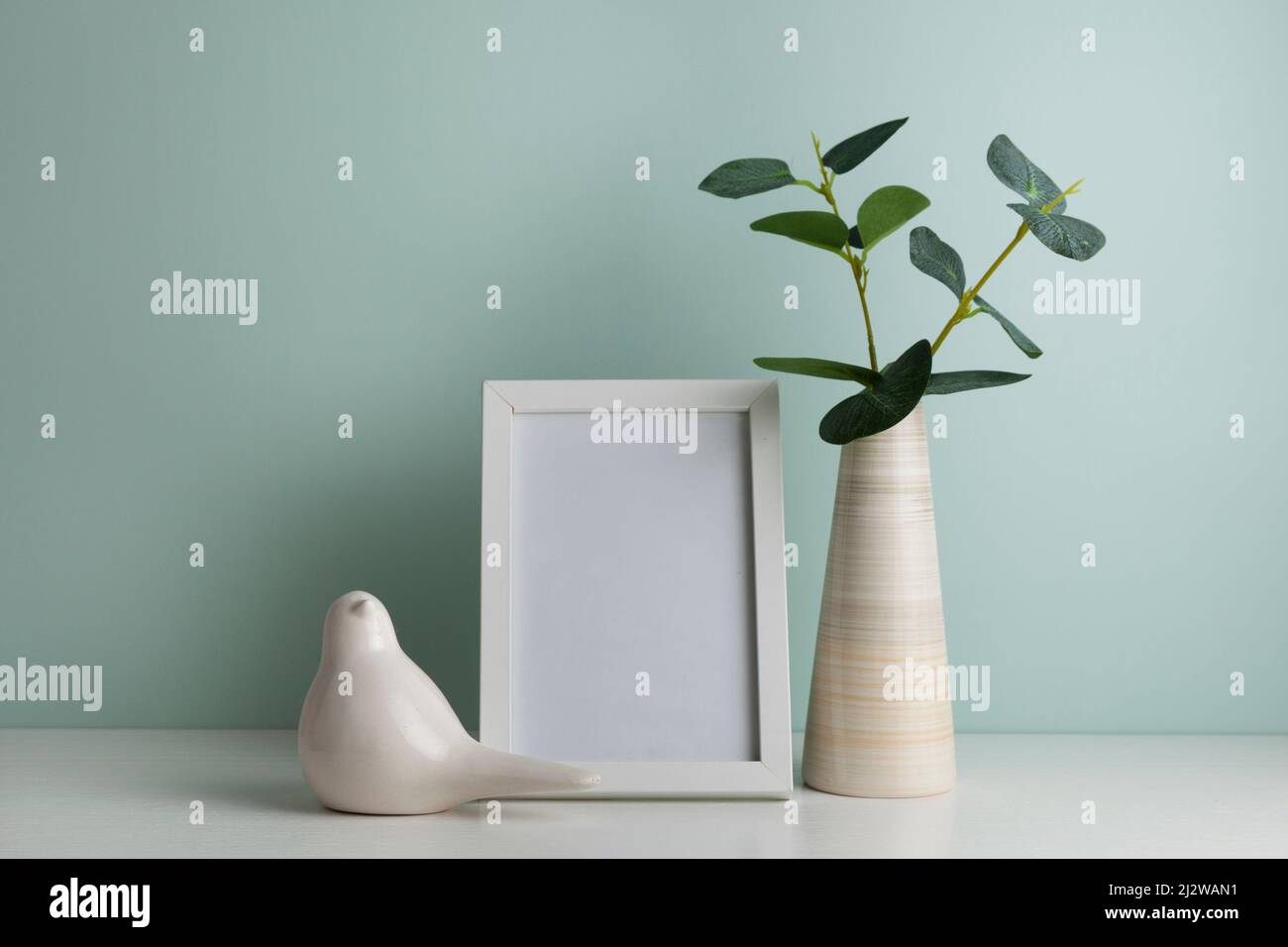 Table de bureau confortable avec vase avec branche verte, oiseau en céramique et cadre photo. Hygge, style boho, salon scandinave Banque D'Images