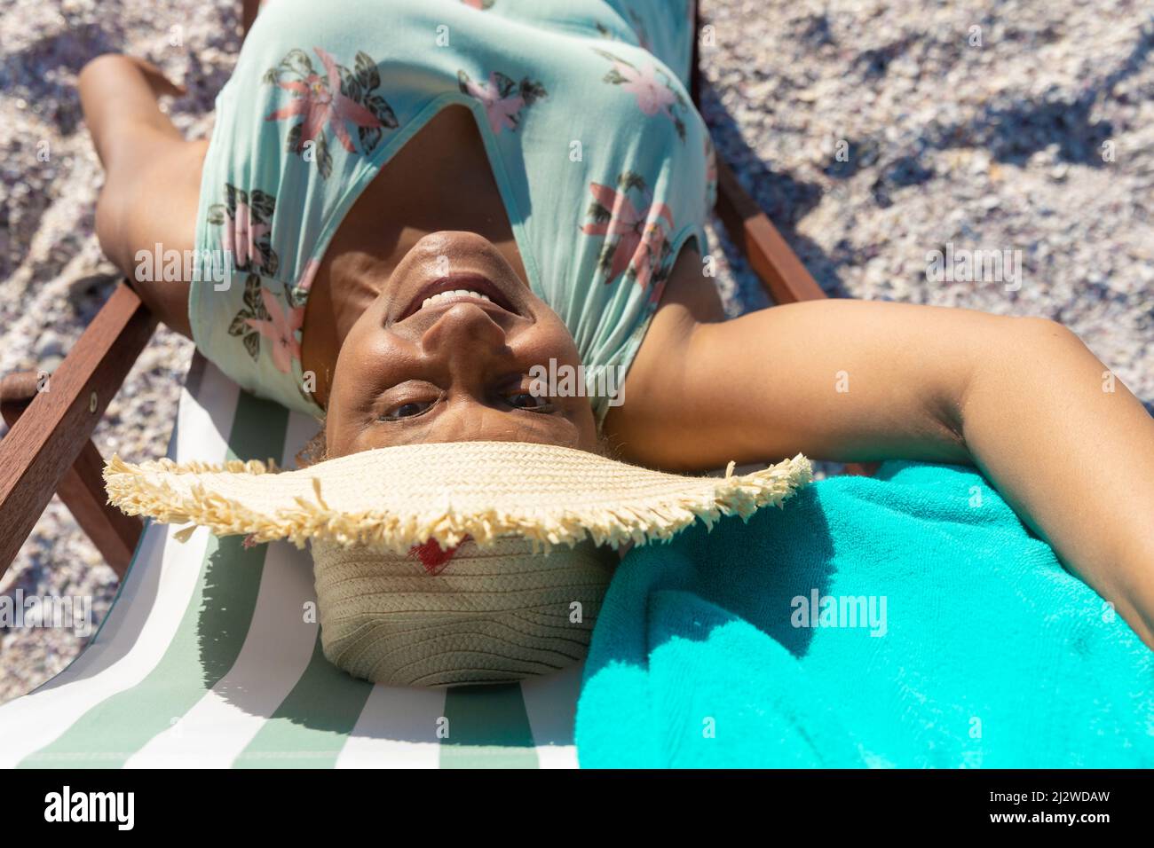 Portrait en grand angle d'une femme afro-américaine souriante prenant le selfie sur une chaise pliante à la plage Banque D'Images