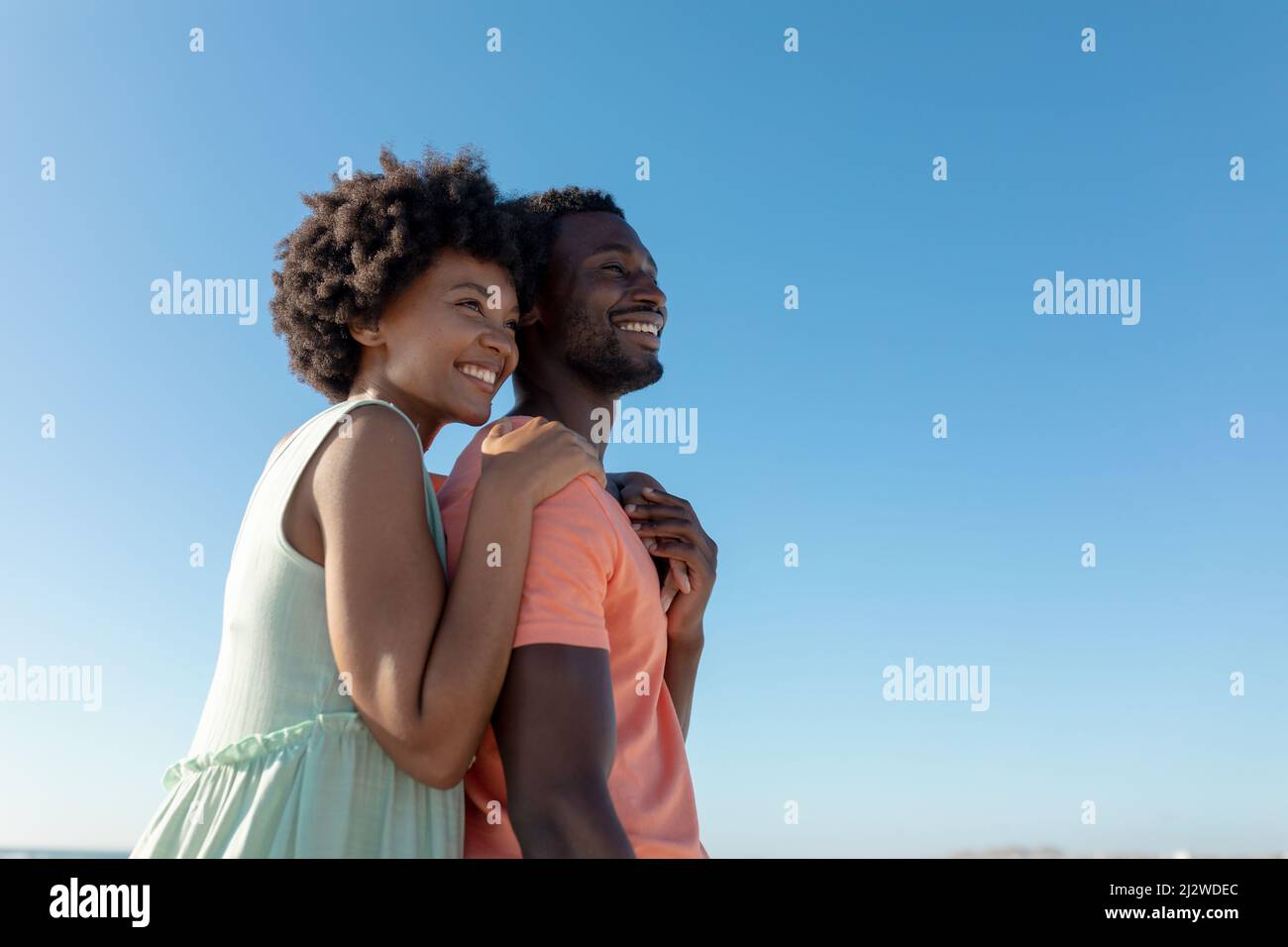 Couple afro-américain souriant debout tout en regardant loin contre le ciel bleu clair avec l'espace de copie Banque D'Images