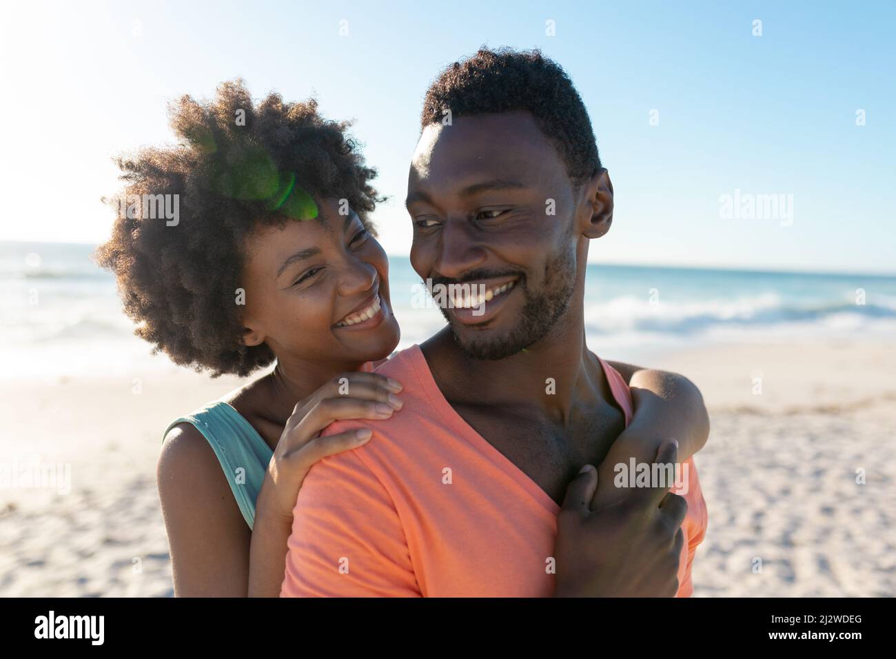 Bonne femme afro-américaine embrassant petit ami de derrière à la plage le jour ensoleillé Banque D'Images