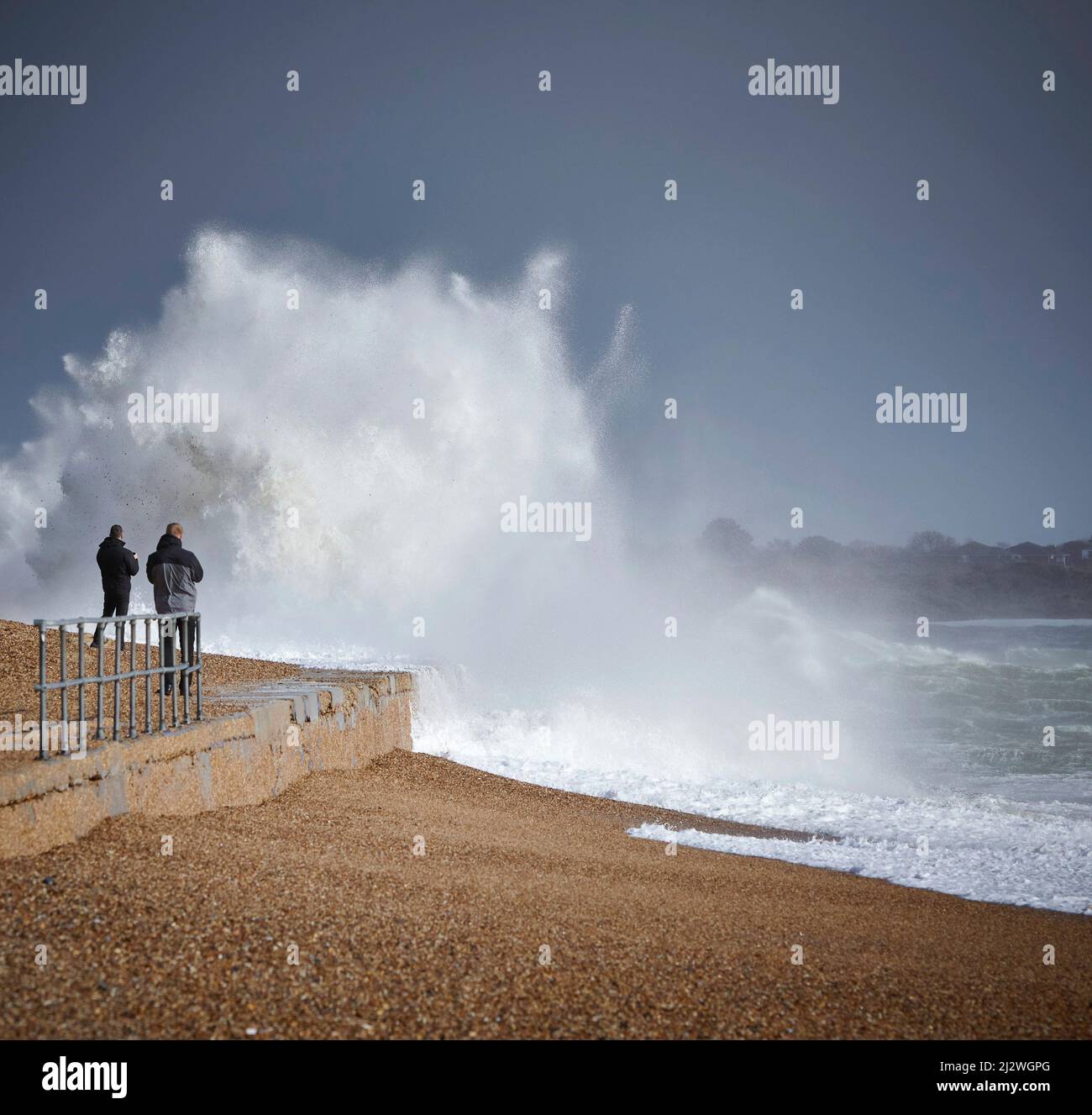 Deux personnes se rapprochent de l'action en prenant des photos de vagues qui se brisent contre la position dure causée par Storm Eunice qui a frappé le Royaume-Uni en février 2022 Banque D'Images