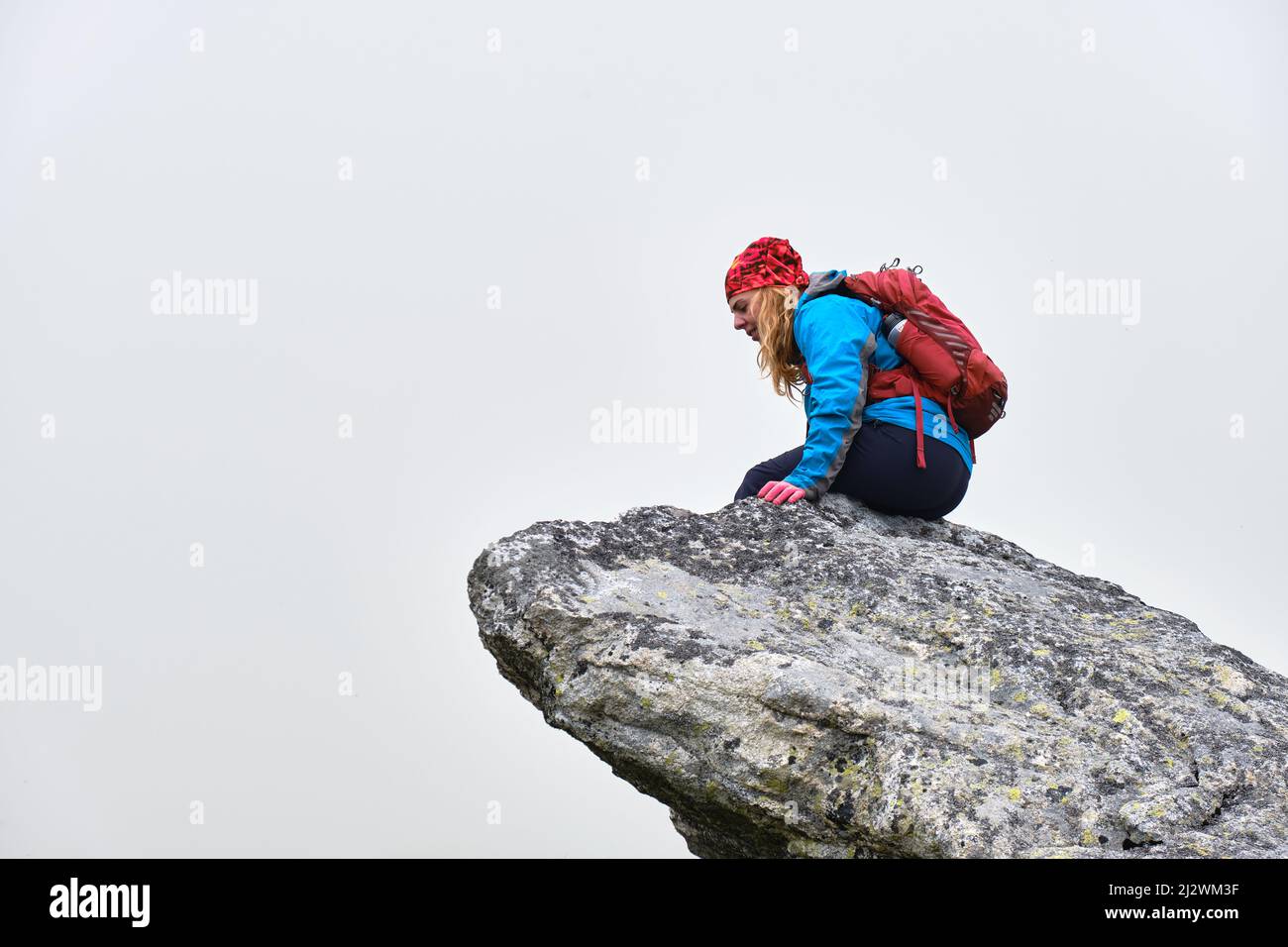 Femme randonneur avec sac à dos rouge se trouve au bord d'une falaise et regarde vers le bas, isolée par le brouillard. Randonnée dans les montagnes des Hautes Tatras en Slovaquie. Banque D'Images