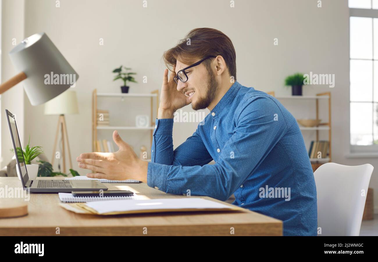 Homme confus et agacé assis au bureau et regardant son ordinateur portable Banque D'Images