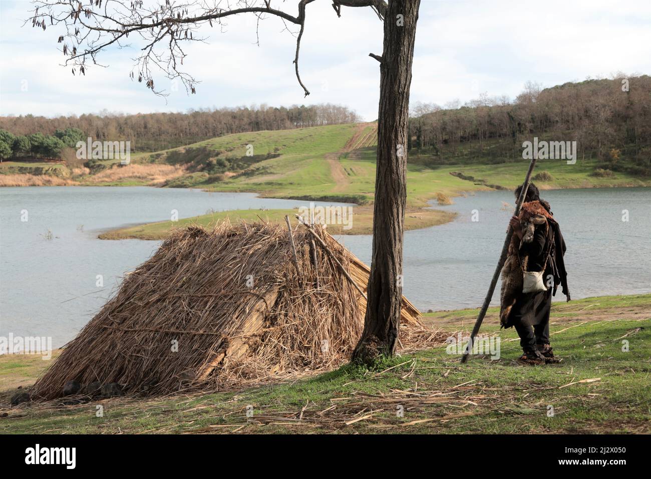 Une tente de chaume au bord du lac. À côté de la tente se trouve un homme en vêtements traditionnels. Banque D'Images