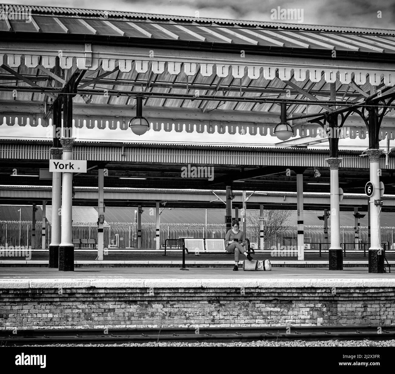 Plate-forme de la gare avec les passagers assis et en attente d'un train. Le toit est un toit historique avec colonnes. Banque D'Images