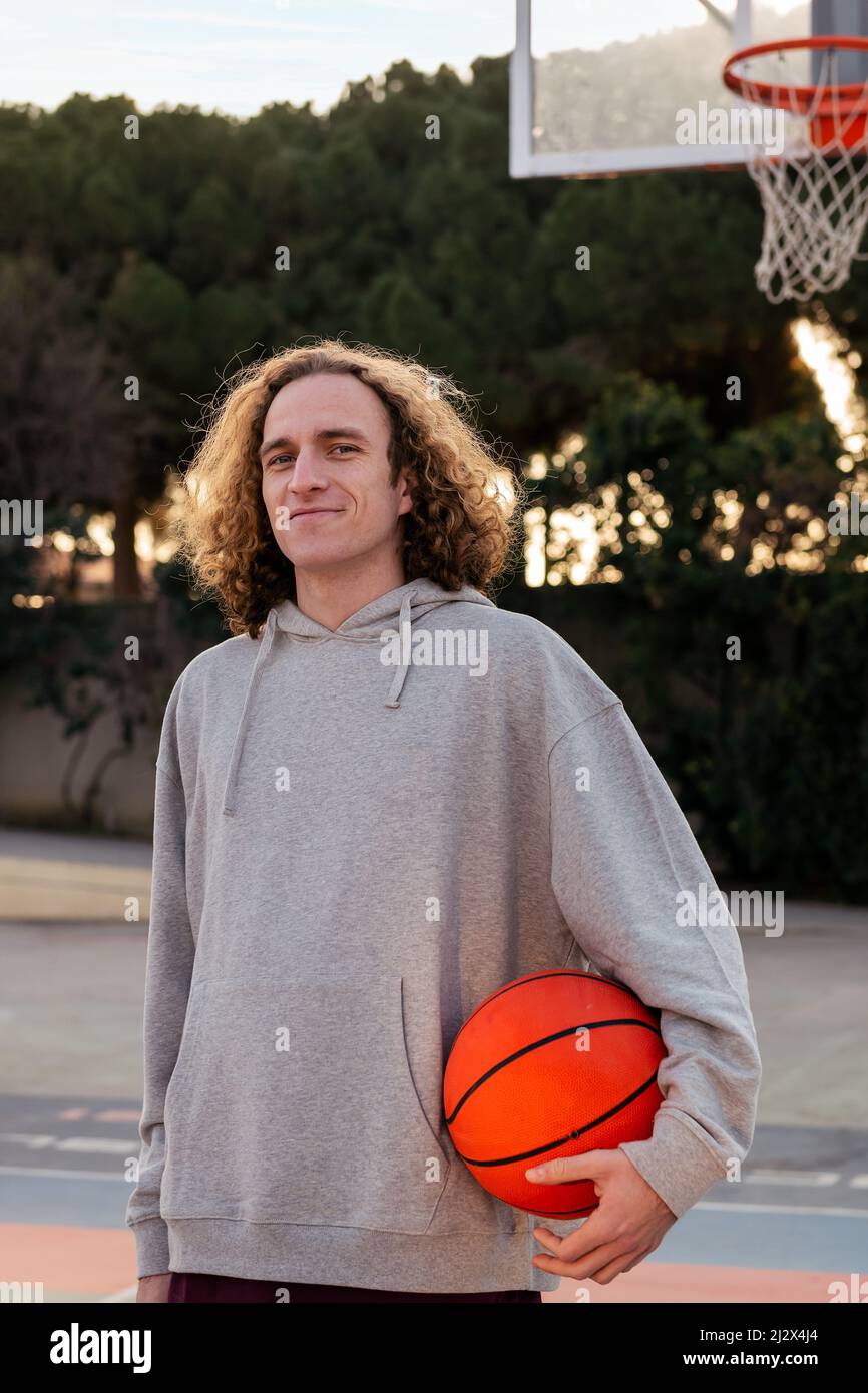 homme caucasien souriant avec une balle sur un terrain de basket-ball dans un parc de ville, concept de sport urbain dans la rue, espace de copie pour le texte Banque D'Images