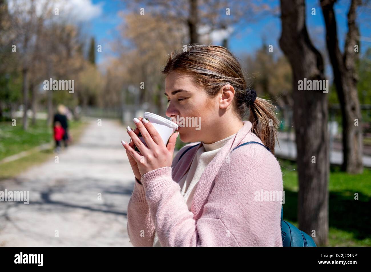 Une jeune femme buvant son café dans le parc par une chaude journée ensoleillée Banque D'Images