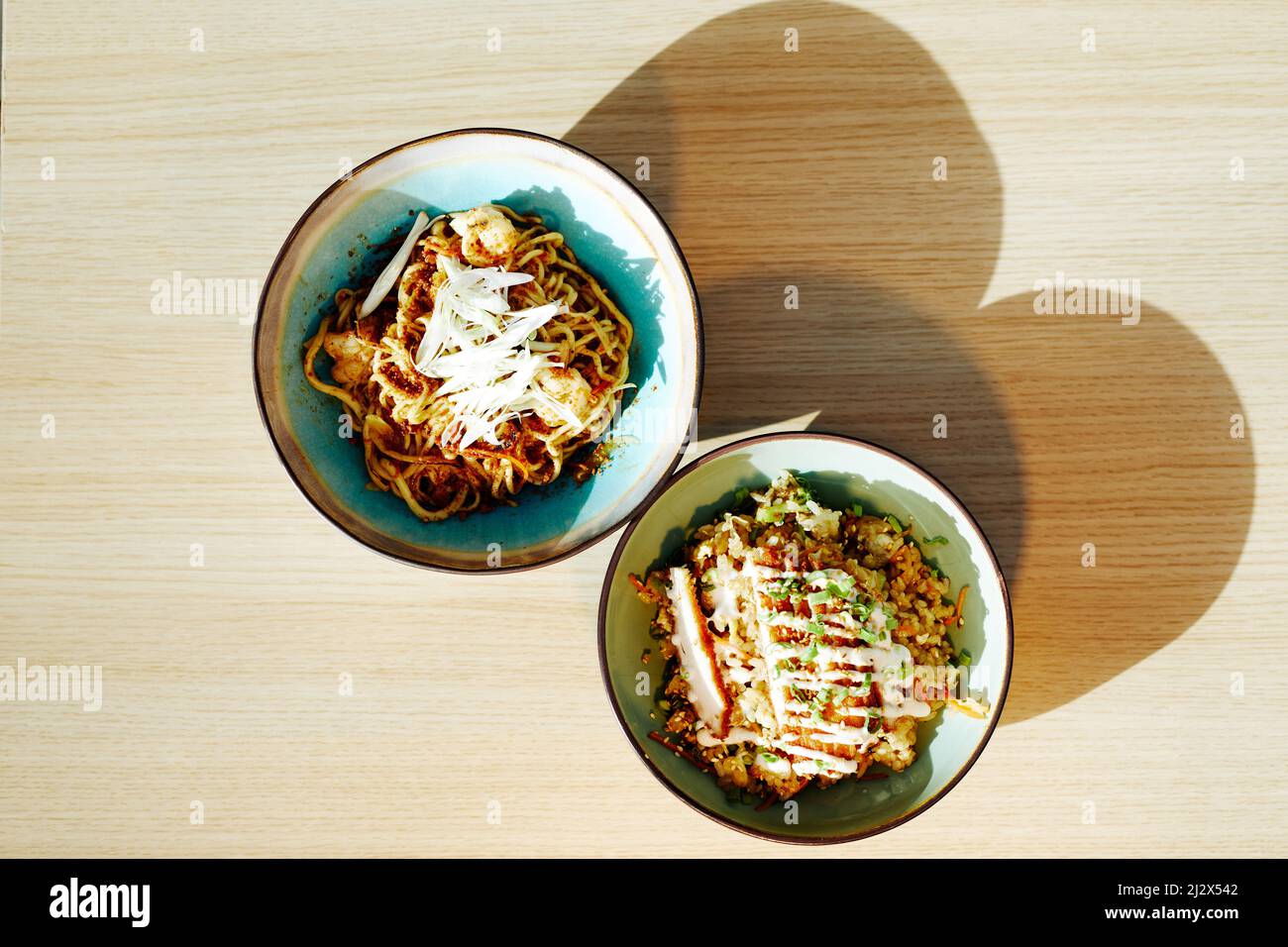 Vue de dessus minimale sur deux bols avec de délicieux plats asiatiques sur une table en bois à la lumière du soleil avec des ombres élevées, espace de copie Banque D'Images