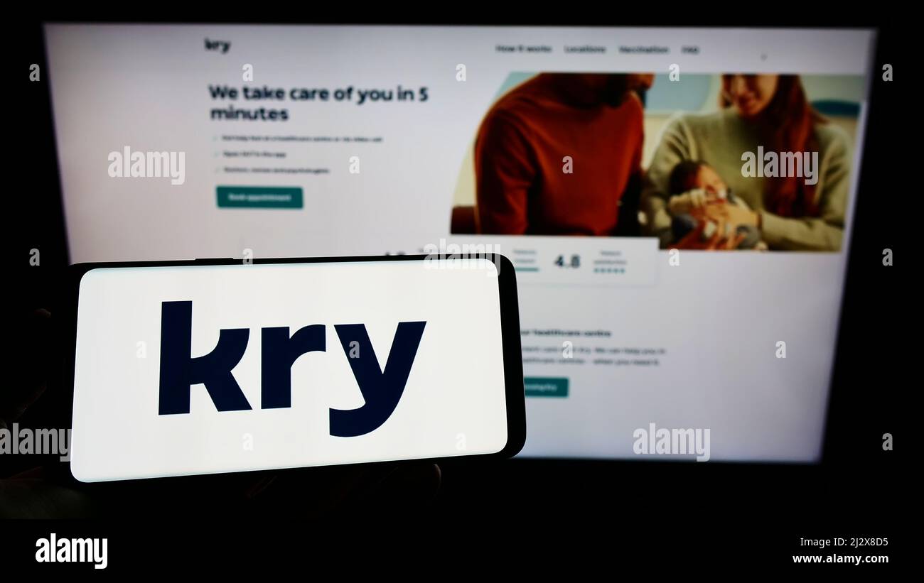 Personne tenant un téléphone portable avec le logo de la société suédoise de soins de santé Kry International AB à l'écran en face de la page Web. Mise au point sur l'affichage du téléphone. Banque D'Images