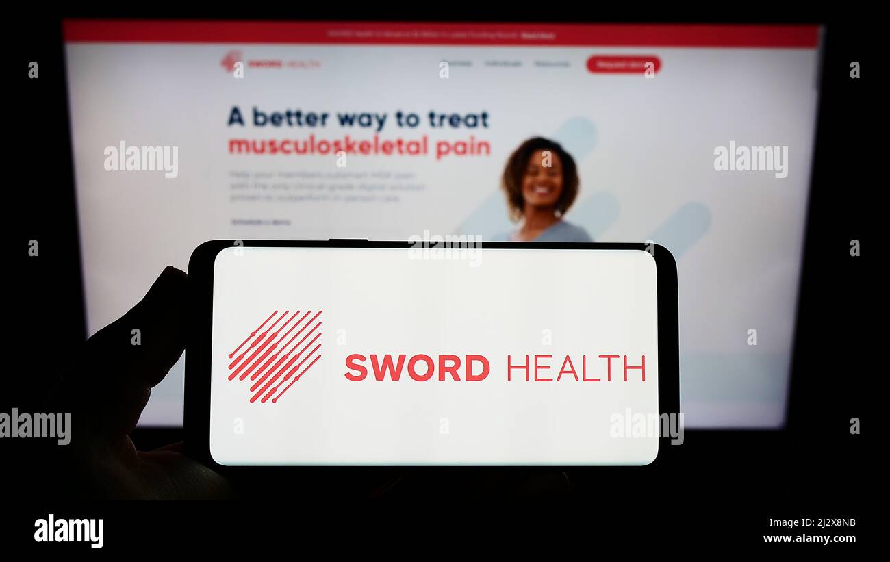 Personne tenant un smartphone avec le logo de l'entreprise de santé électronique SWORD Health Inc. À l'écran devant le site Web. Mise au point sur l'affichage du téléphone. Banque D'Images