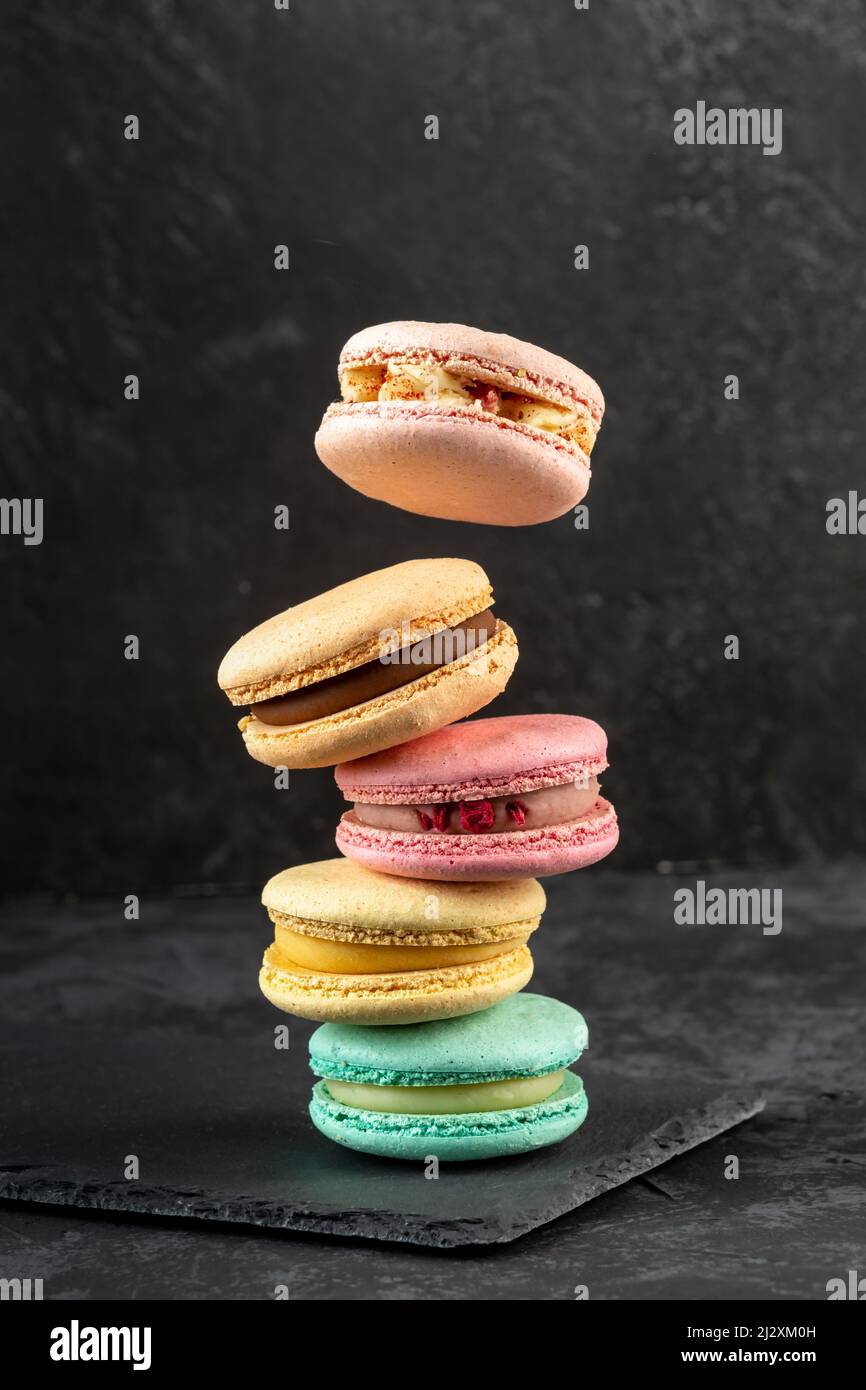 Macarons empilés sur un fond sombre. Délicieux dessert de cuisine française décoré de façon créative sur fond sombre Banque D'Images
