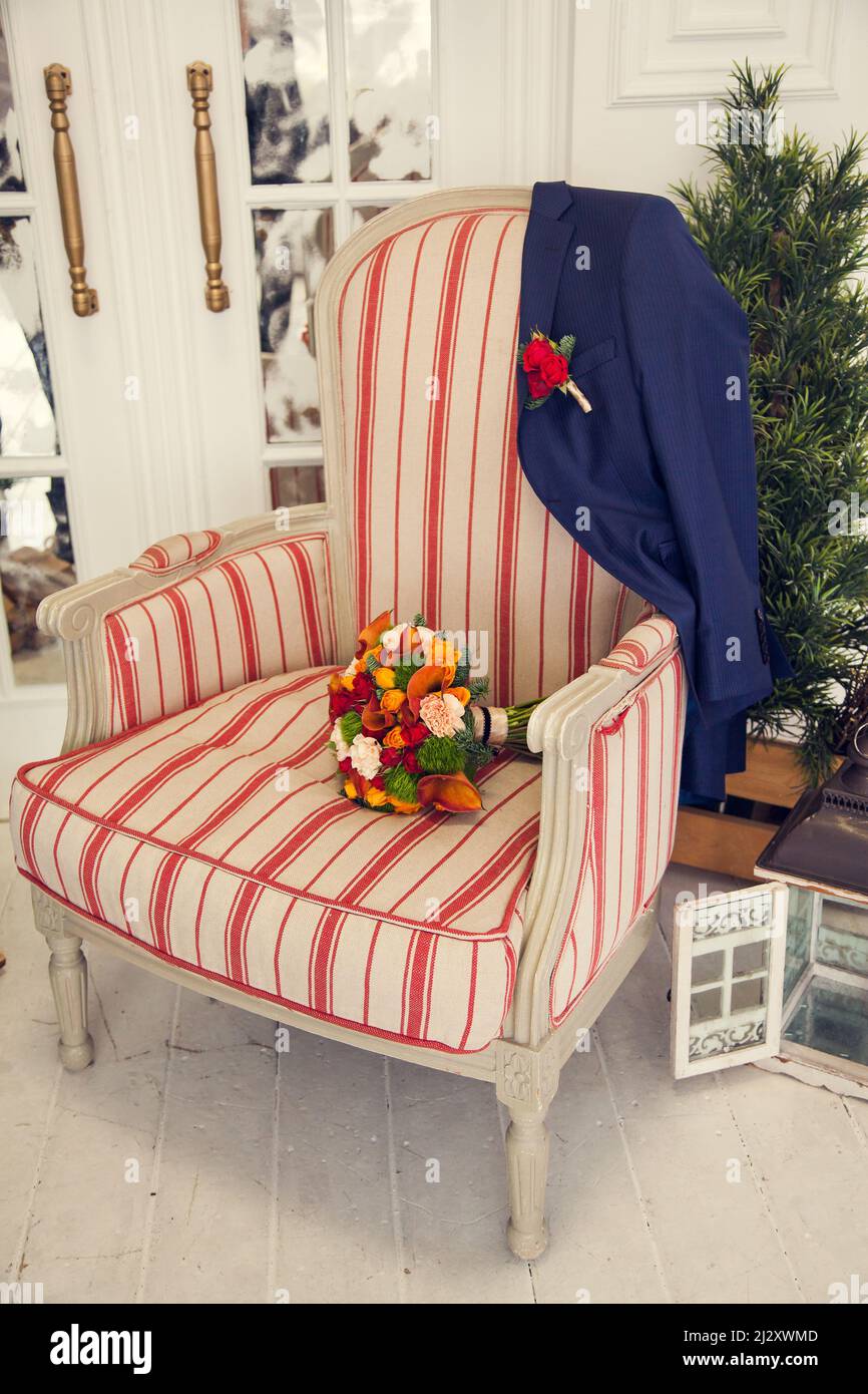 Le bouquet de la mariée et la veste du marié avec une boutonnière sur un ancien fauteuil rembourré dans la chambre à coucher pendant Noël. Banque D'Images