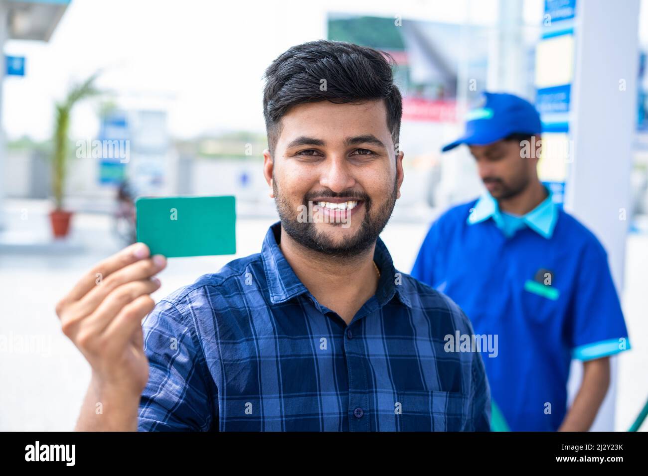 Souriant clients montrant la carte verte vide en regardant la caméra à la pompe à essence - concept de l'identité de l'employé, offre sur la carte de carburant, promotion et publicité. Banque D'Images