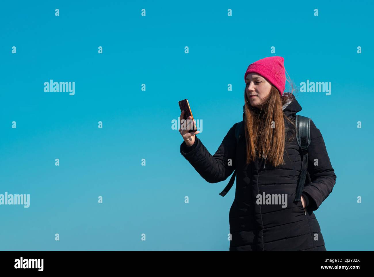 Jeune femme confiante en chapeau rose avec smartphone à la main appelant des amis marchant sur fond de ville ciel bleu. Une jolie petite fille à l'extérieur Banque D'Images