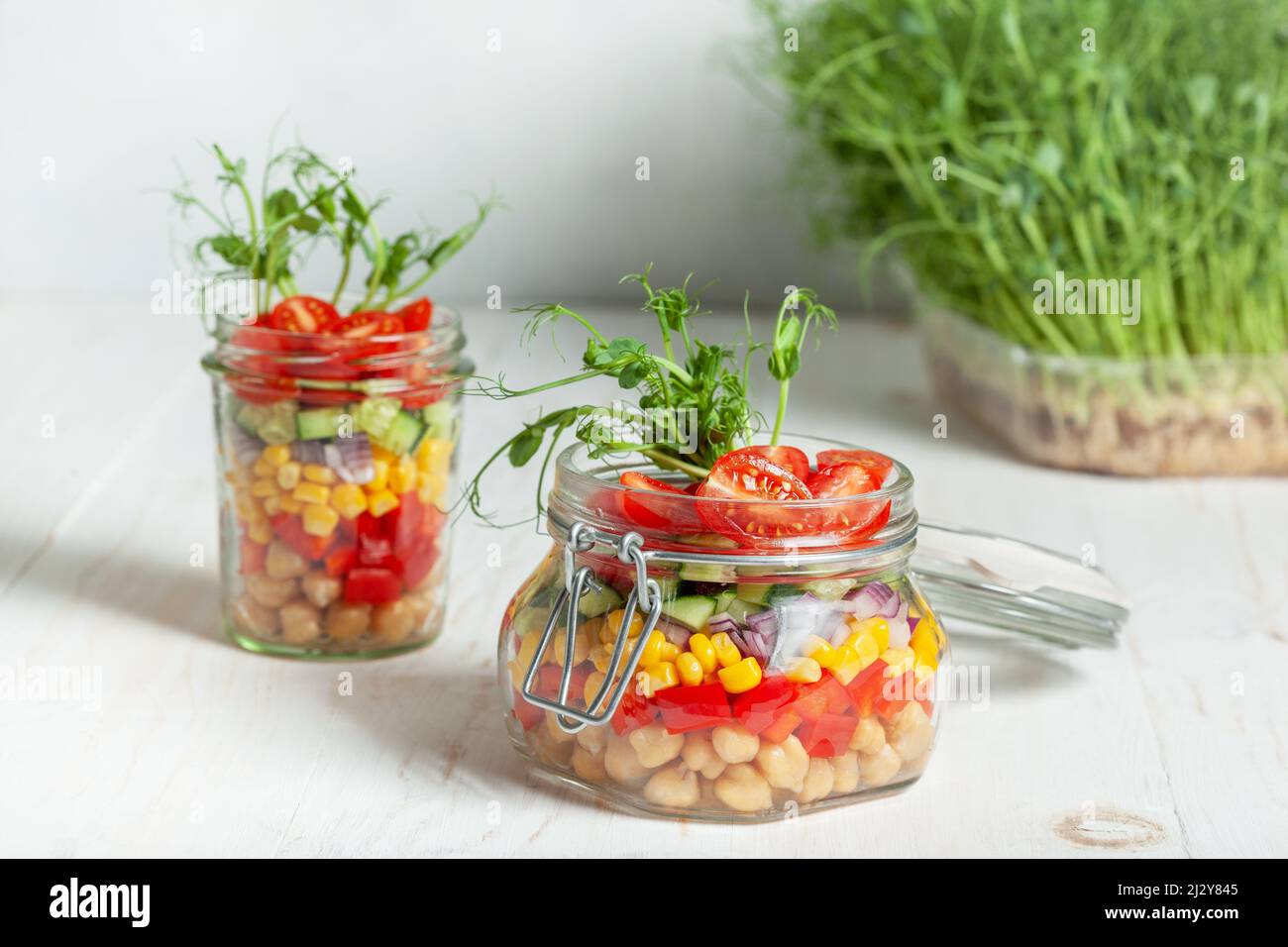 salade maison saine dans un pot. salade végétarienne avec pois chiches et légumes, pousses de pois dans des pots sur fond de bois blanc Banque D'Images