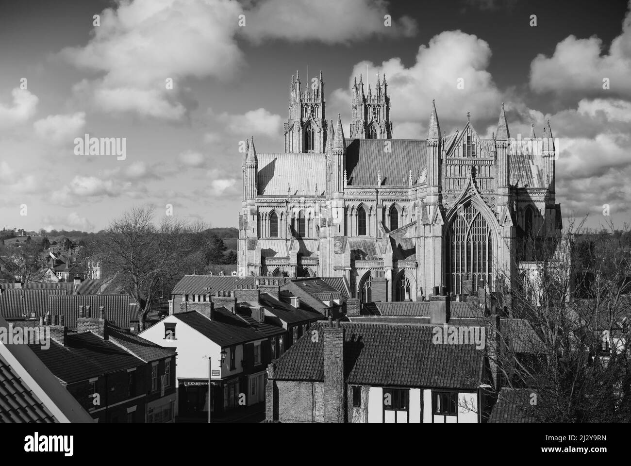 Vue en hauteur de l'ancienne cathédrale (église) flanquée de maisons et entourée d'un ciel bleu avec vue sur les nuages depuis le parking local. Beverley, Royaume-Uni. Banque D'Images