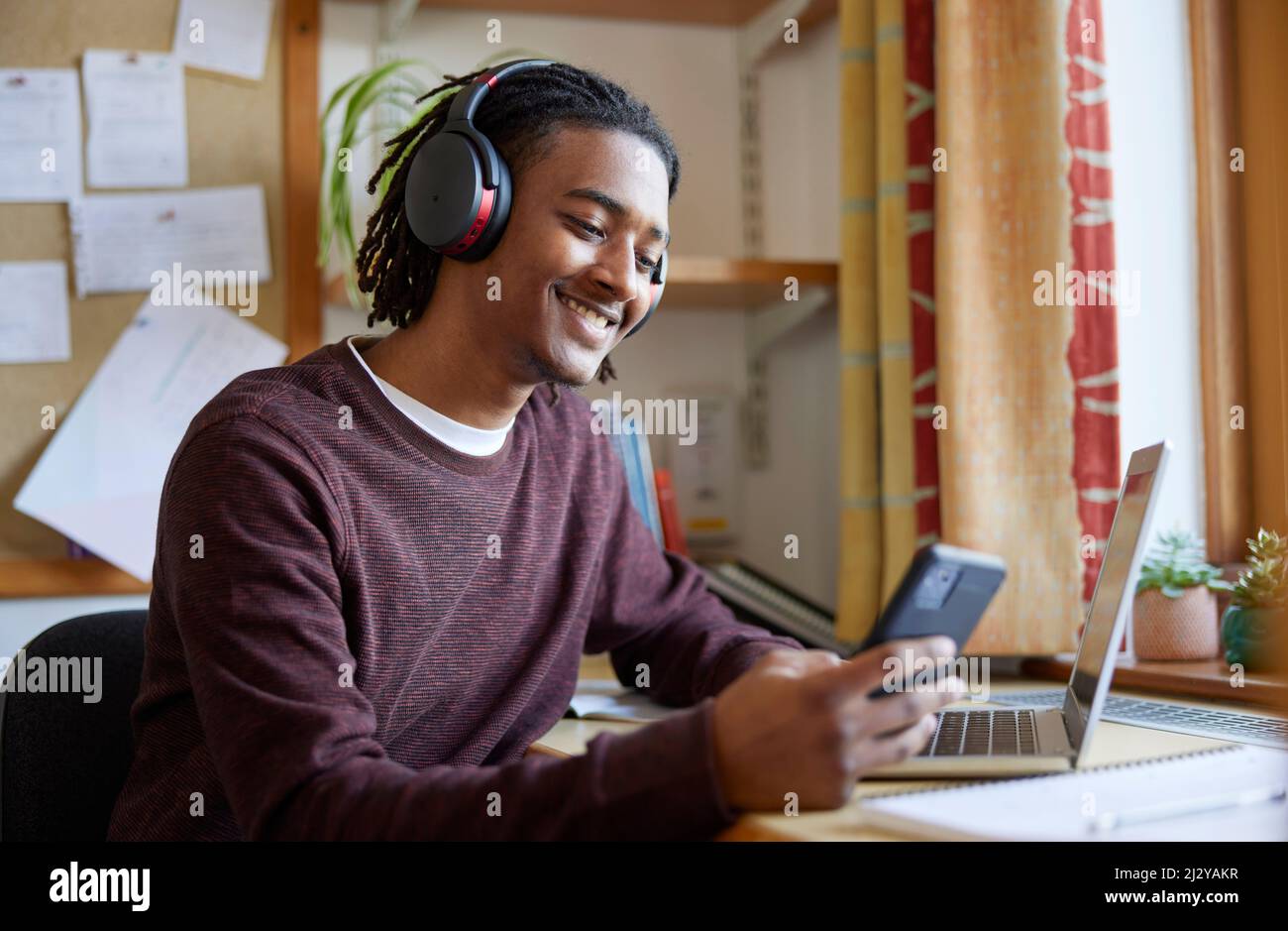 Un étudiant de l'université ou de l'université porte un casque sans fil avec un ordinateur portable au bureau dans la chambre, avec vue sur le téléphone mobile Banque D'Images