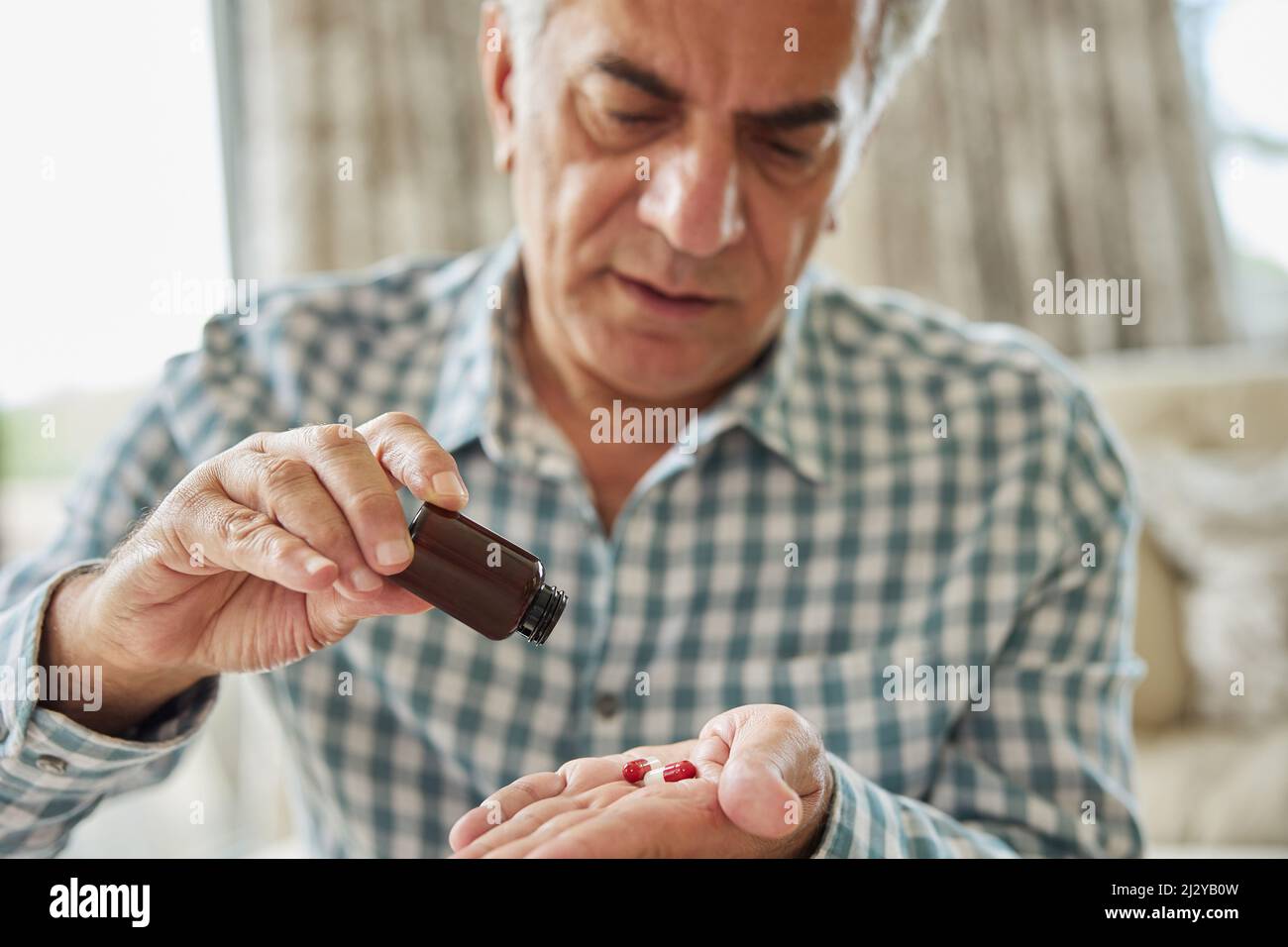 Homme mature assis sur un canapé à la maison prenant des médicaments Banque D'Images