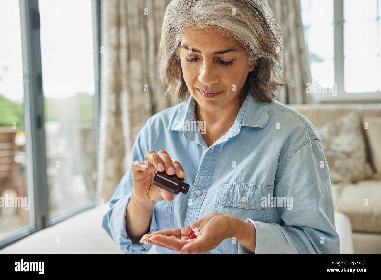 Femme mature assise sur un canapé à la maison prenant des médicaments Banque D'Images