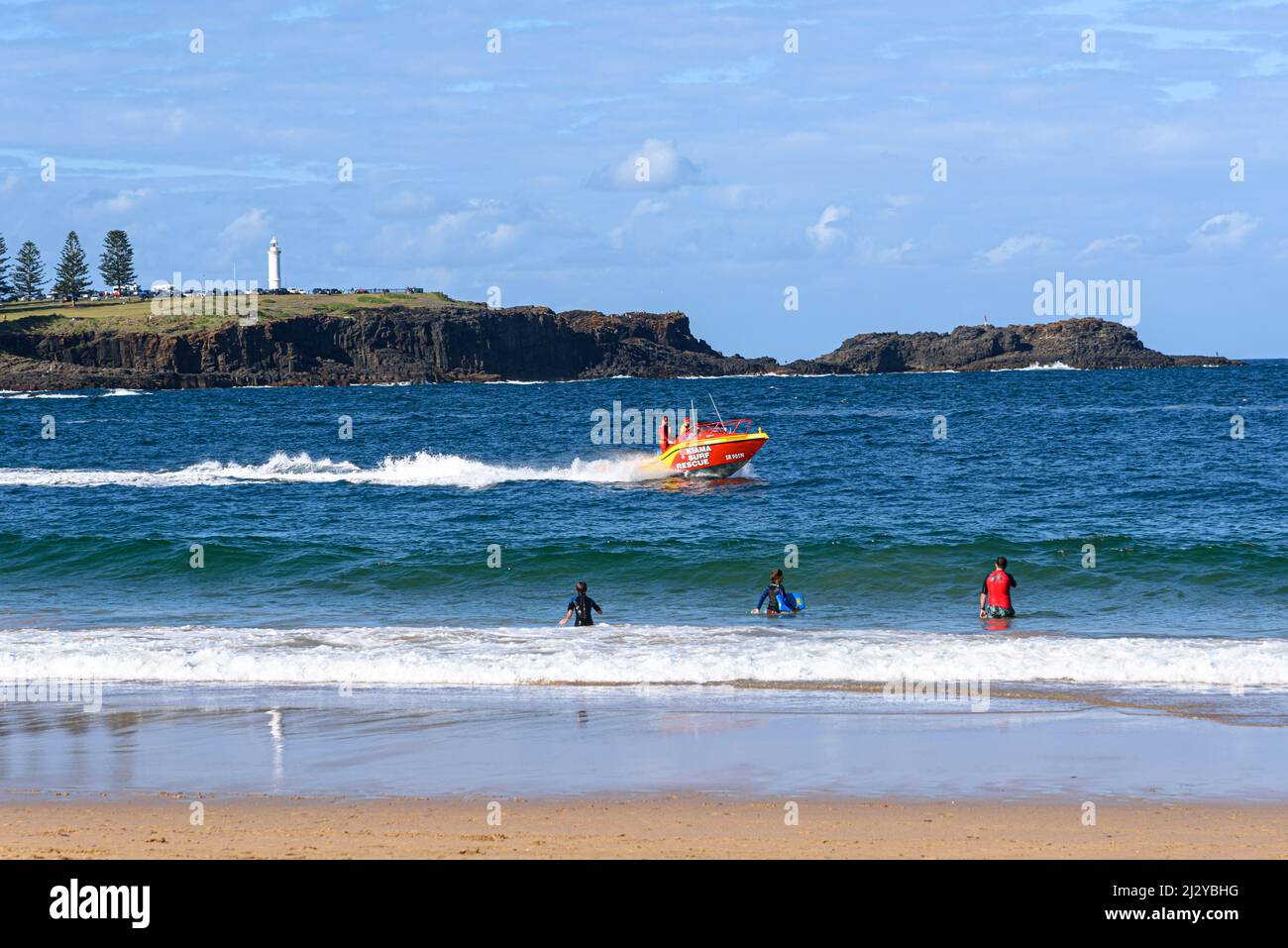 Les gens de Kendalls Beach regardent un bateau de sauvetage Kiama Surf aller près de la rive avec Blowhole point en arrière-plan Banque D'Images