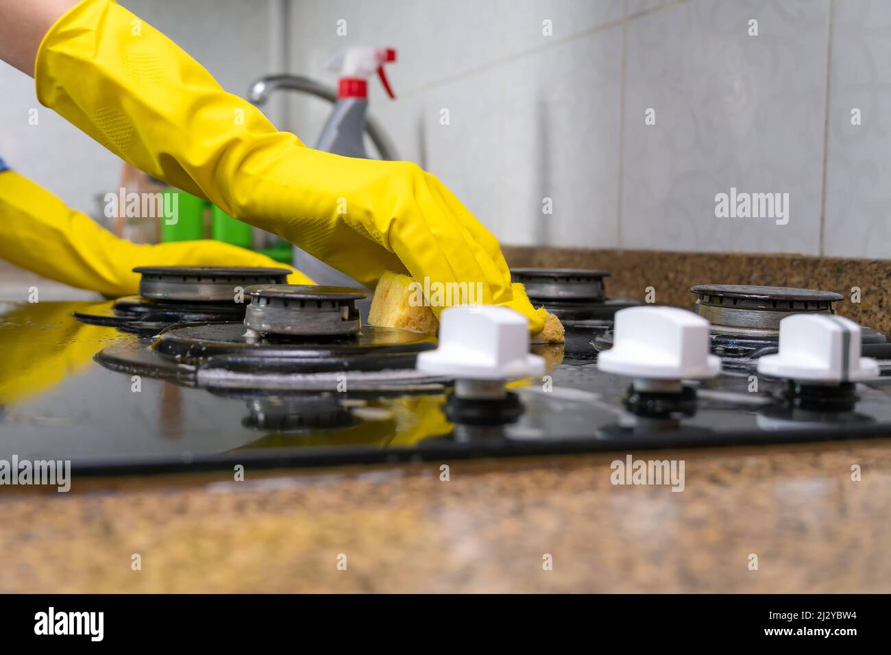 Gros plan de la main d'une femme en gants jaunes, lavage de la cuisinière avec un agent nettoyant et une éponge Banque D'Images