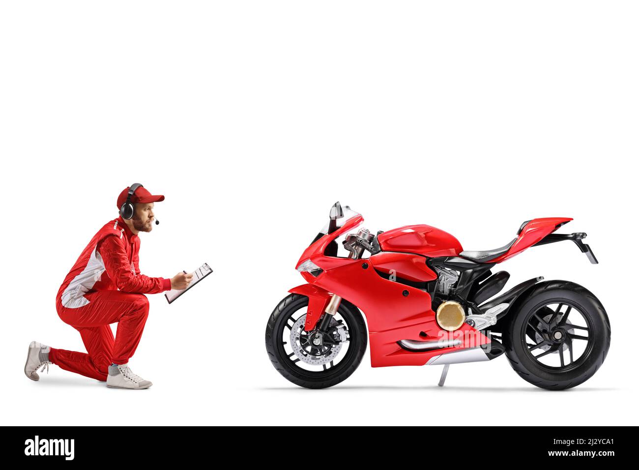 Membre d'une équipe de course à genoux devant une moto et écrivant sur un presse-papiers isolé sur fond blanc Banque D'Images
