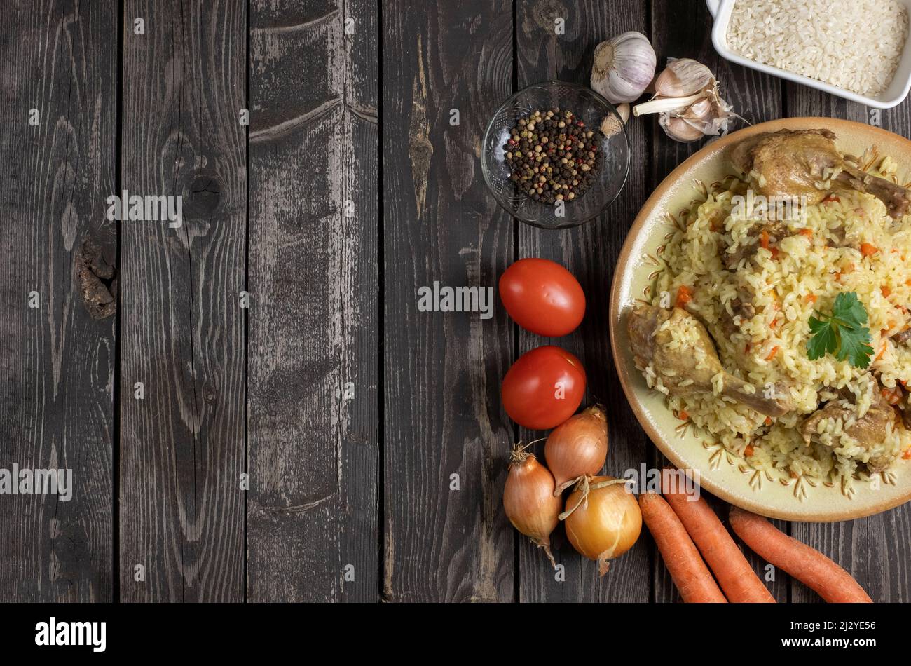 Pilaf ouzbek avec canard. Riz avec morceaux de viande de canard avec ingrédients de cuisson, oignons, carottes, ail, poivrons et tomates. Plat sur bois sombre Banque D'Images