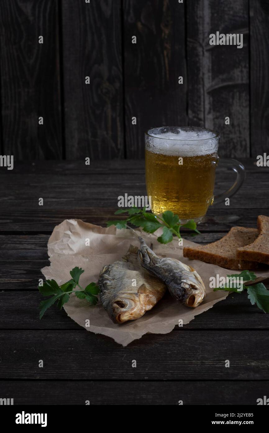 poisson fumé salé et séché avec bière ambrée sur fond de bois sombre et pain sur table Banque D'Images