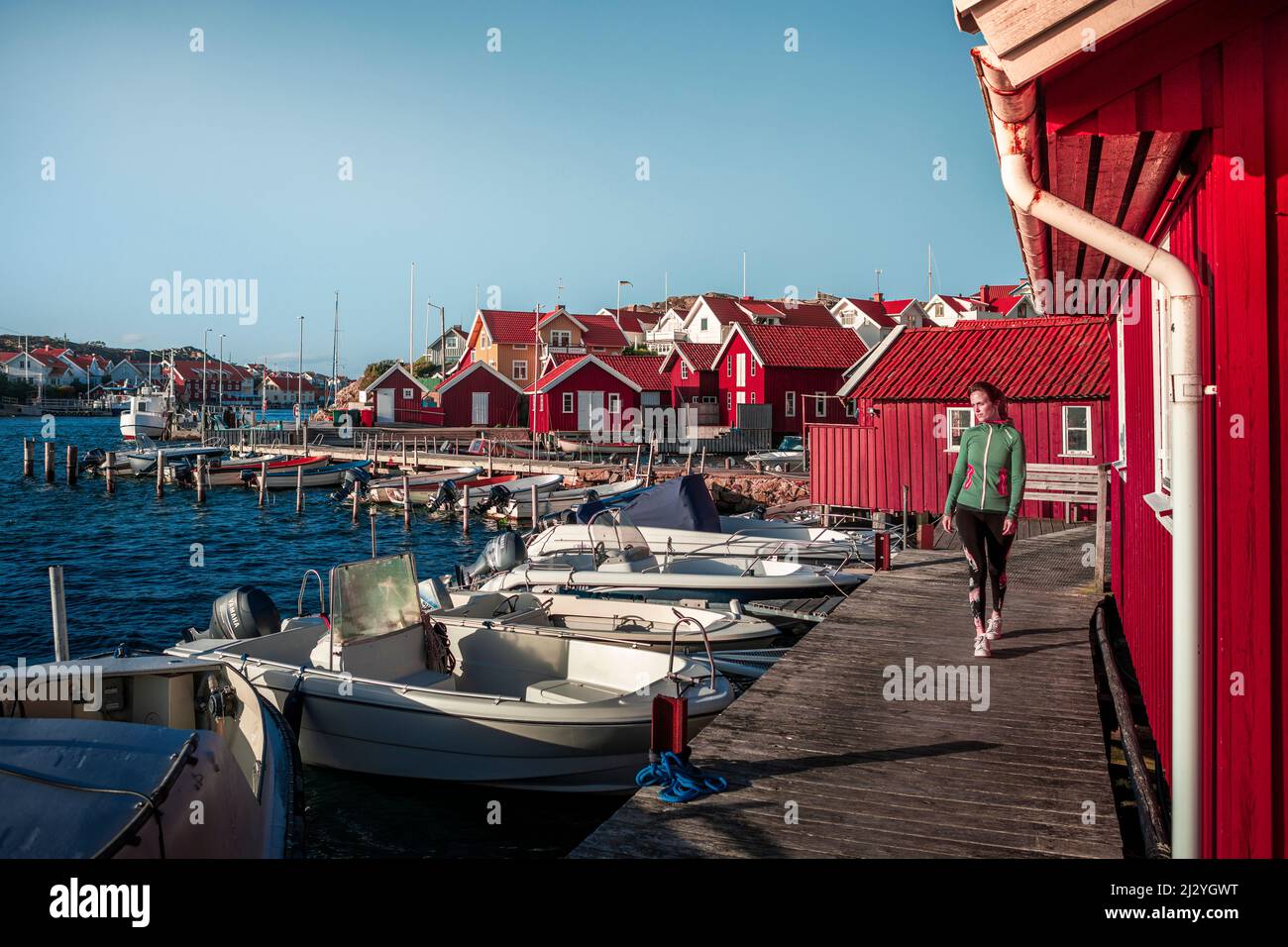 Femme au port dans le village de Kyrkesund sur l'archipel de Tjörn sur la côte ouest de la Suède, ciel bleu avec le soleil Banque D'Images