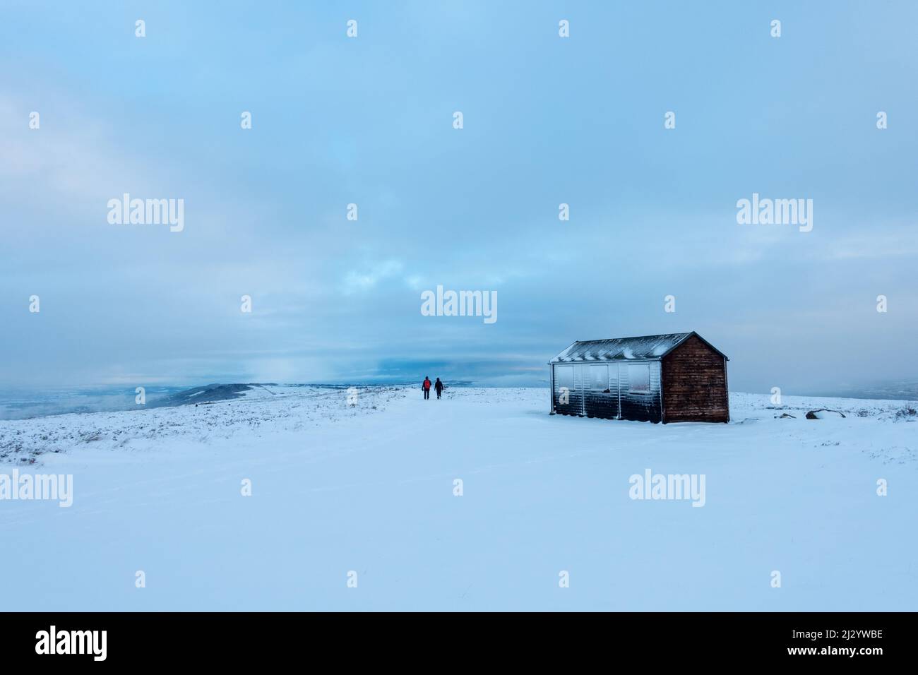 Deux personnes marchant sur un sentier enneigé, devant une cabane de tir de mésse sur Burley Moor, West Yorkshire, Angleterre, Royaume-Uni Banque D'Images