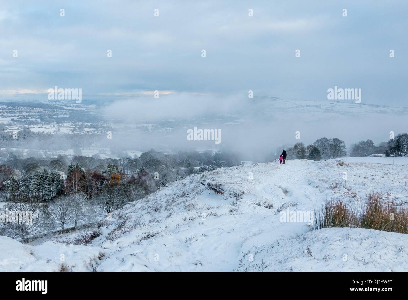 Parent et enfant profitant d'une promenade enneigée par temps venteux avec une inversion de nuages sur Burley Moor, West Yorkshire, Angleterre, Royaume-Uni Banque D'Images