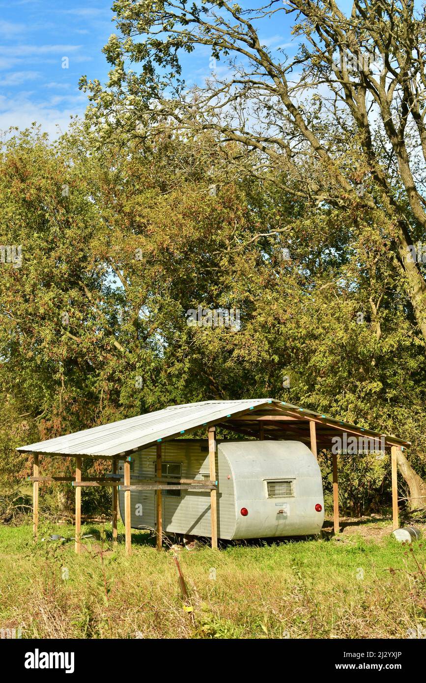 Remorque de camping vintage en métal argenté, branchée et élégante, garée sous un toit en métal protecteur dans un emplacement isolé, sur une colline de ferme sous les arbres, Osseo, Wisconsin, États-Unis Banque D'Images