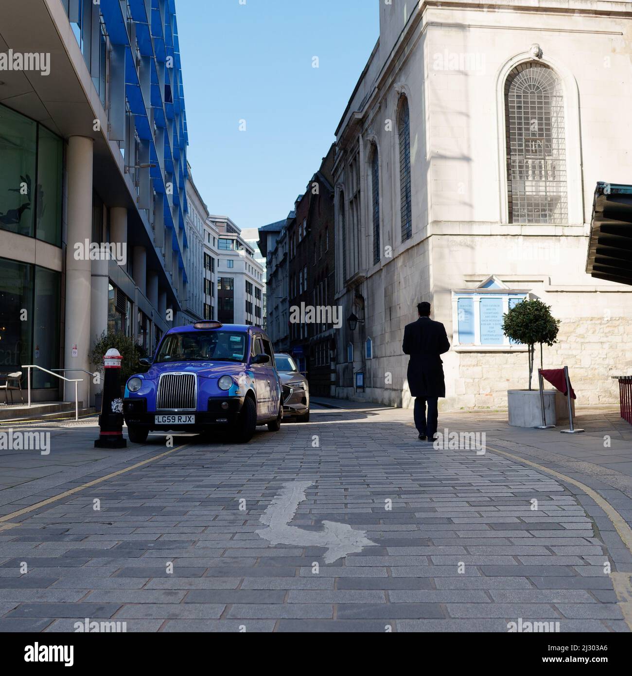 Londres, Grand Londres, Angleterre, mars 19 2022 : l'homme en silhouette marche à côté d'un taxi bleu dans la City de Londres. Road Sign en premier plan. Banque D'Images