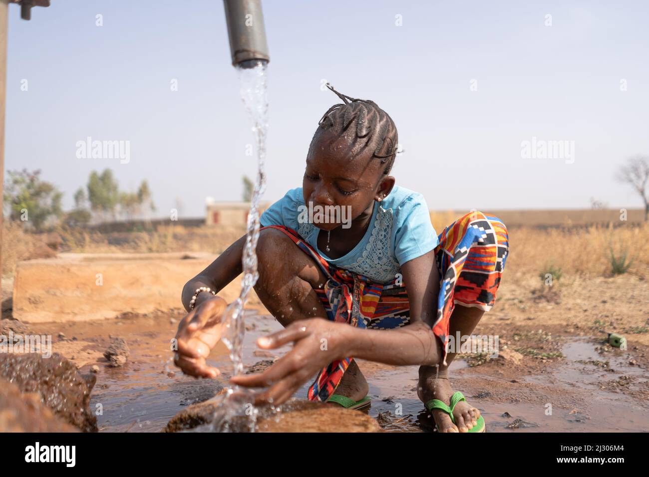 Une fille africaine assoiffée se rafraîchit avec de l'eau potable fraîche d'un robinet de village ; concept de pénurie d'eau, pénurie d'eau pancontinentale Banque D'Images