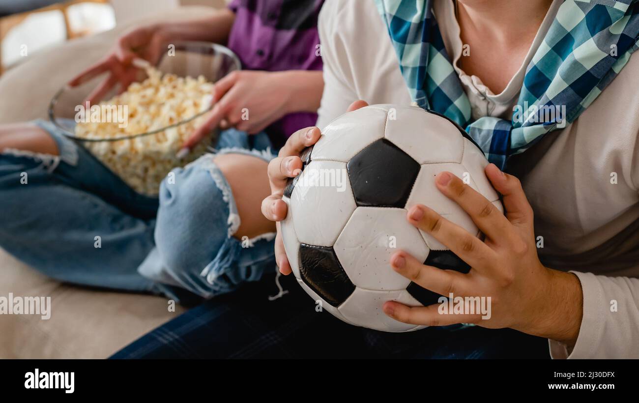 Gros plan sur les mains d'un homme caucasien inconnu tenant le ballon de football tout en regardant le match à la maison Banque D'Images