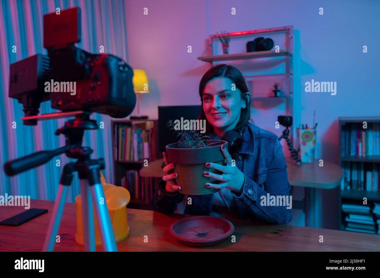 Belle femme hispanique devant une caméra vidéo enregistrant un blog dans son studio avec des lumières rouges et bleues à l'intérieur de sa maison. La diffusion de son jardini Banque D'Images