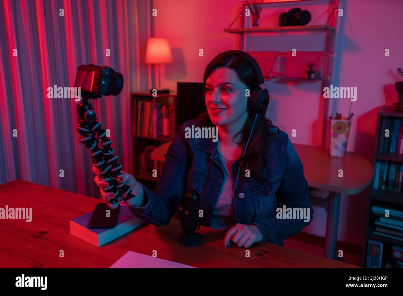 Belle femme hispanique devant une caméra vidéo enregistrant un blog dans son studio avec des lumières rouges et bleues à l'intérieur de sa maison. Diffuser son commentaire Banque D'Images