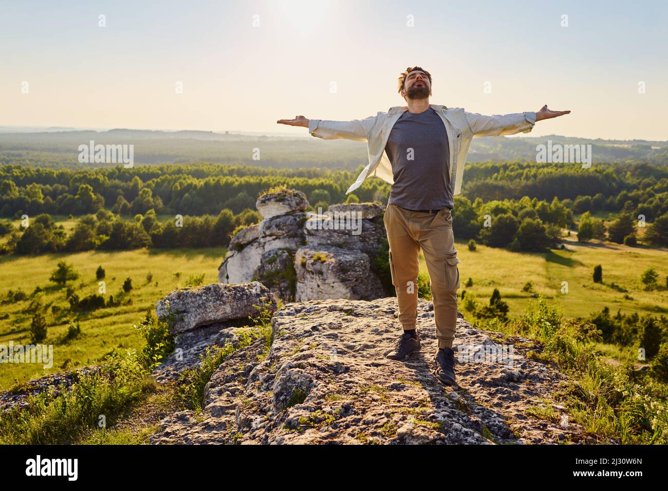 Jeune homme debout au sommet de la montagne par beau temps avec les bras larges ouverts en profitant de la randonnée estivale Banque D'Images