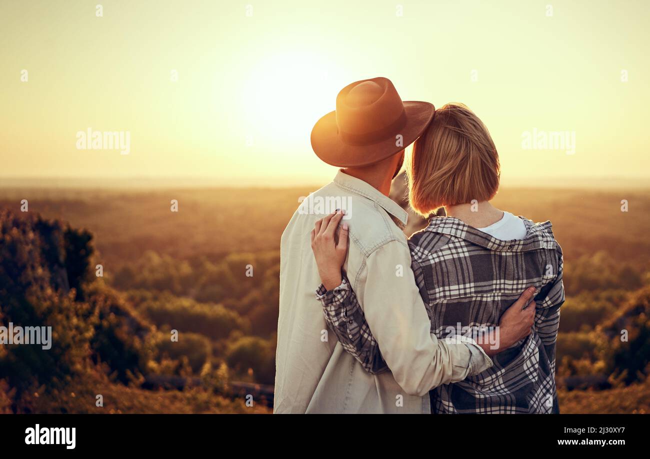 Un jeune couple regarde le coucher du soleil s'embrassant dans la nature pendant la randonnée estivale Banque D'Images